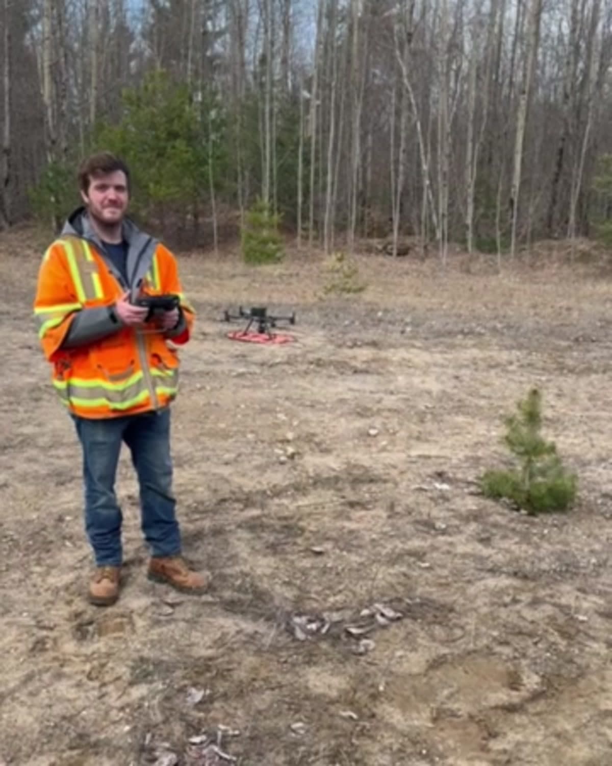 A surveyor operating a mapping drone beside its landing pad in a cleared field